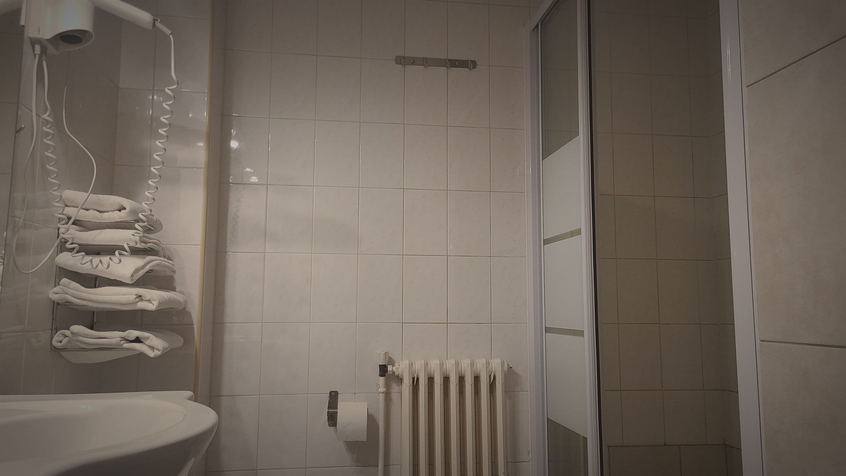A bathroom with a white sink, a towel rack with folded towels, a hairdryer, and a white radiator.