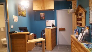 A small, compact room with a wooden desk, a chair, a wooden cabinet, and a small wooden shelf with books. There is a white door and a window with a calendar on the wall. - Hôtel Restaurant Glaizette (L'Argentiere-la-Bessee)