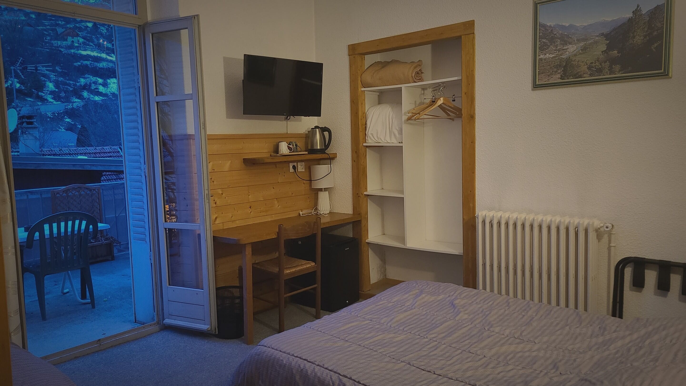 Een slaapkamer met een bed, een bureau, een stoel, een televisie, een radiator en een kledingkast.
