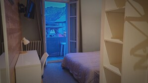 A bedroom with a bed, a desk, and a chair. There is a window with a view of a mountain and a building. - Hôtel Restaurant Glaizette (L'Argentiere-la-Bessee)
