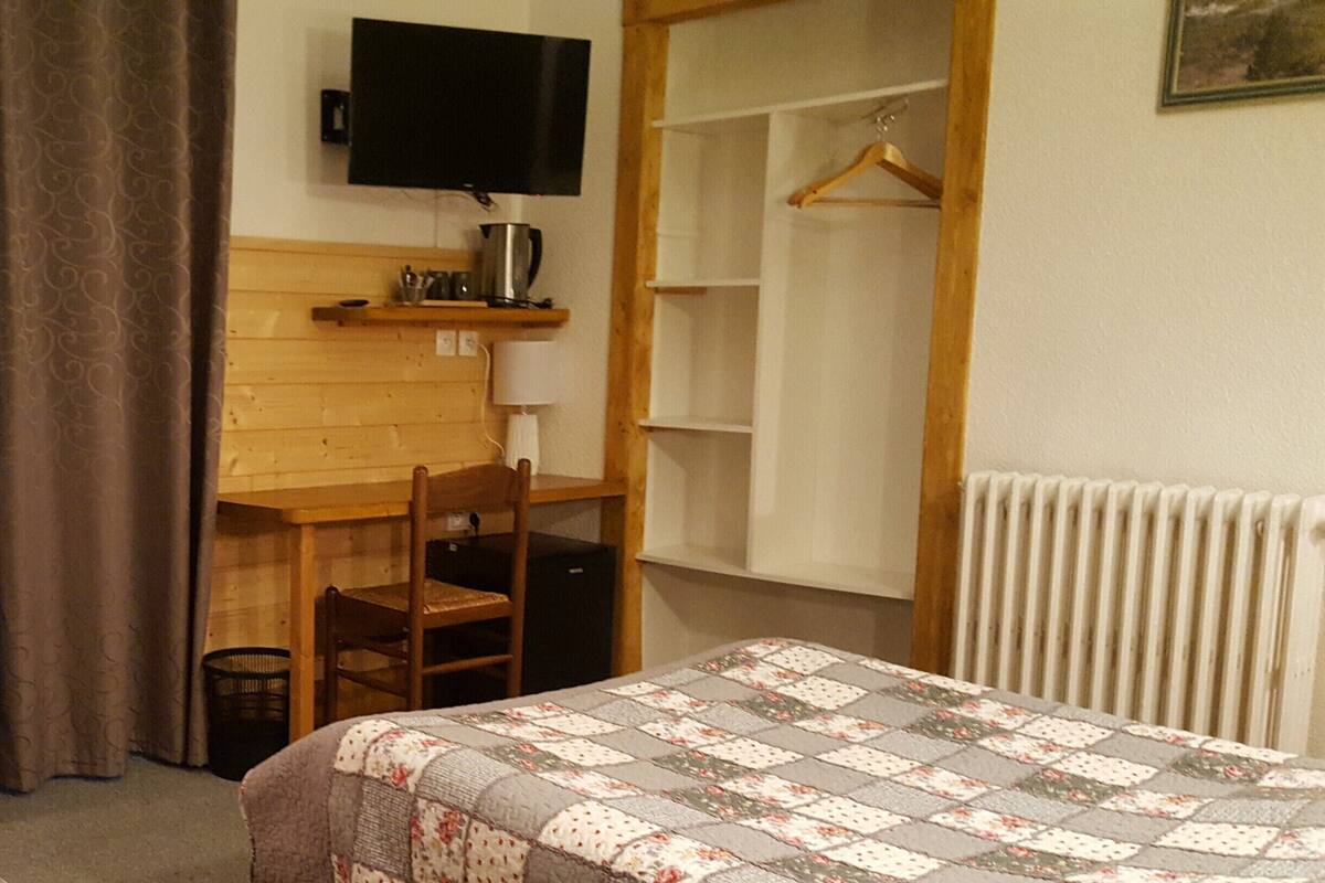 A bedroom with a bed, a desk, a chair, a television, and a radiator.