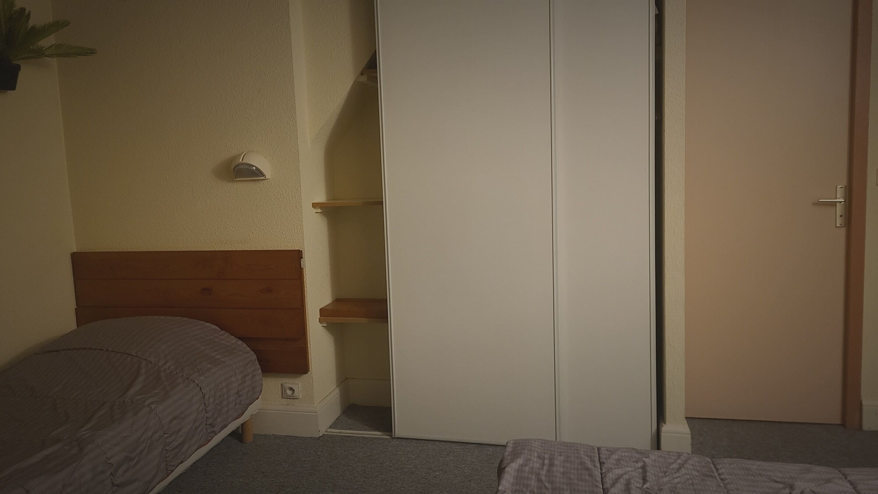 A bedroom with a wooden headboard bed, a white wardrobe, and a small shelf unit.