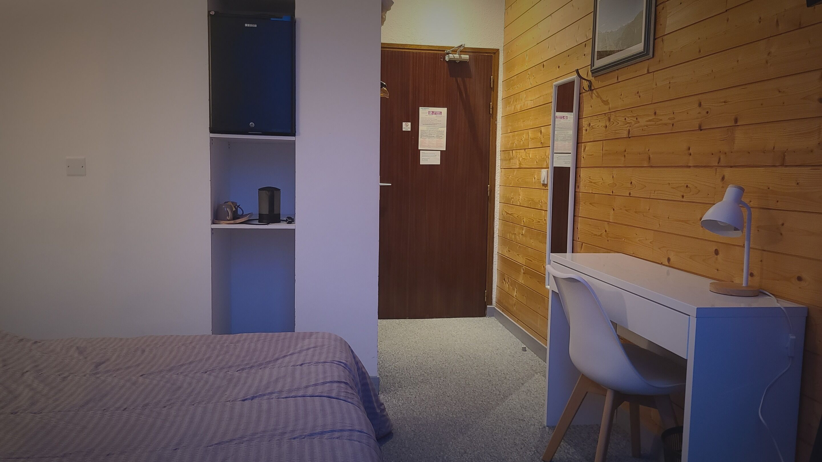 A bedroom with a bed, a desk, and a chair. There is a door leading to another room.