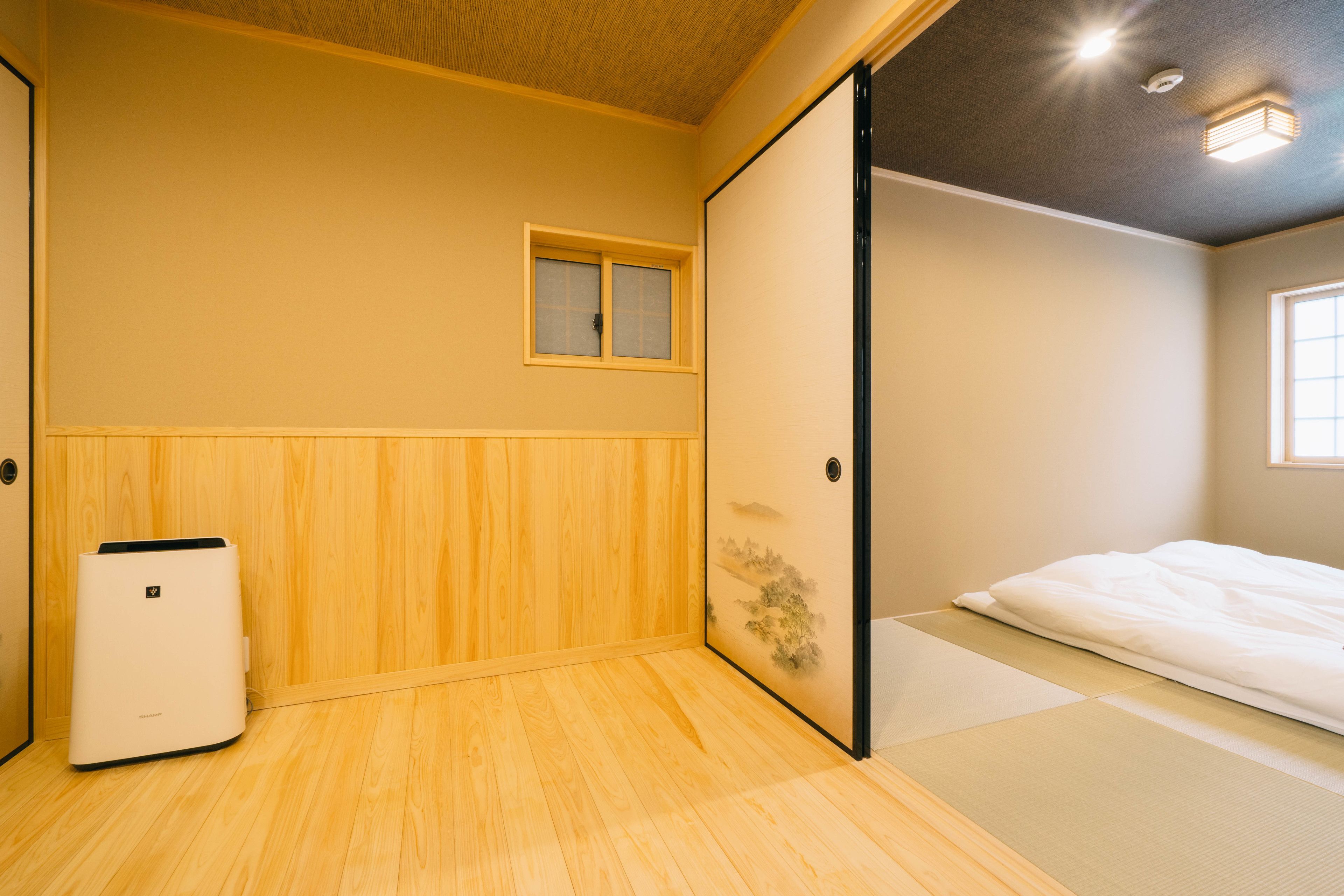 A room with a wooden floor, a bed with white bedding, a small window, and a wall-mounted heater.
