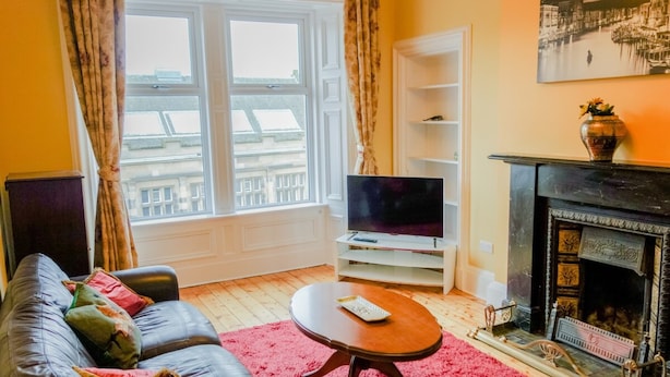 A living room with a sofa, a television, a fireplace, and a window with curtains.