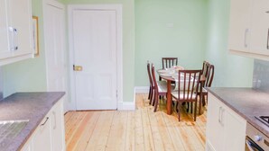 A kitchen with wooden flooring, white cabinets, and a dining table with chairs.