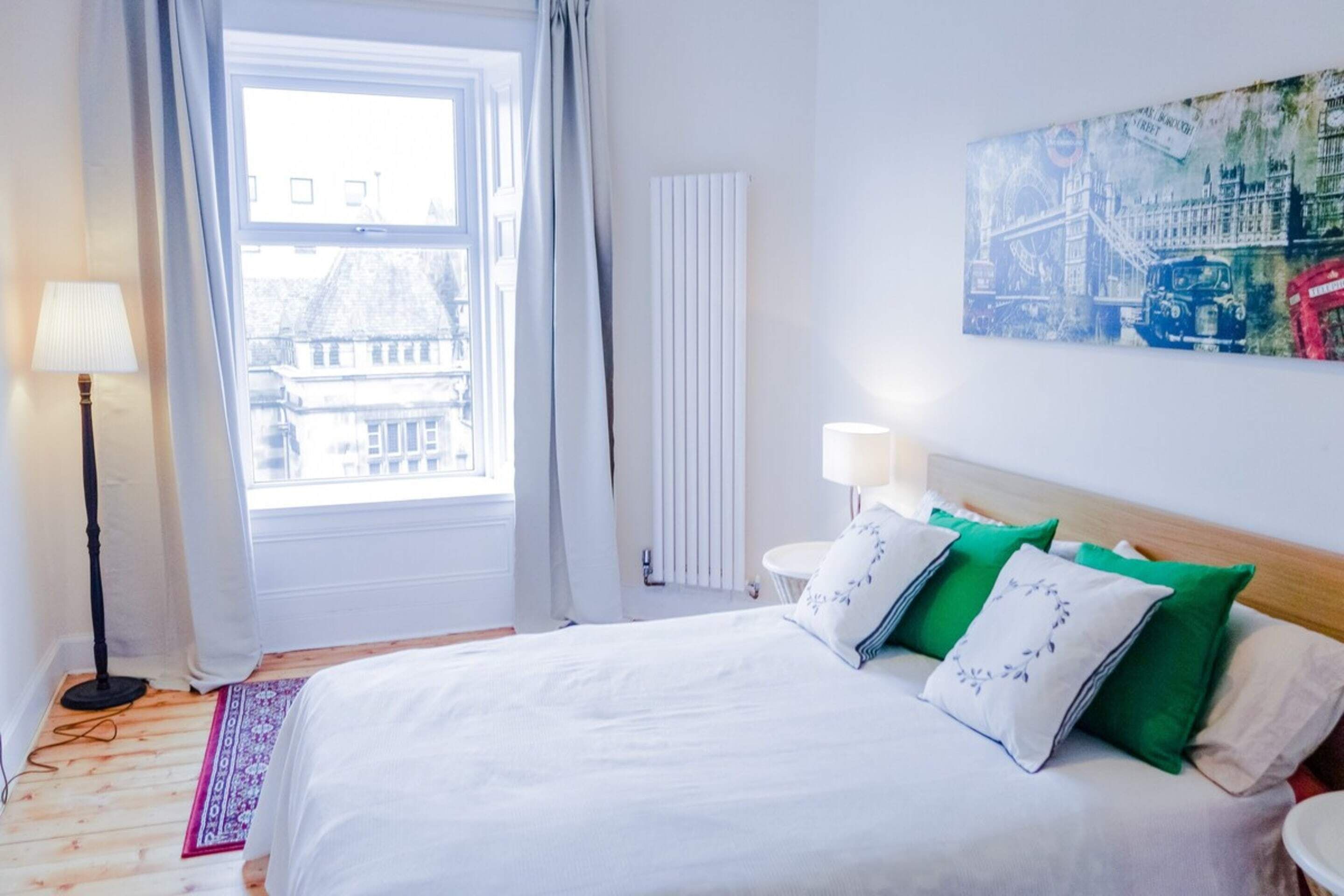 Une chambre d’hôtel avec un grand lit, une fenêtre avec des rideaux, un radiateur et une œuvre d’art accrochée au mur.