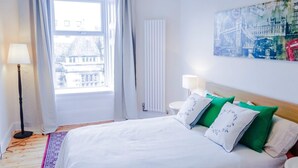 A hotel room with a large bed, a window with curtains, a radiator, and a wall-mounted artwork.