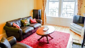 A living room with a leather sofa, a red rug, a coffee table, a TV, and a window with curtains.