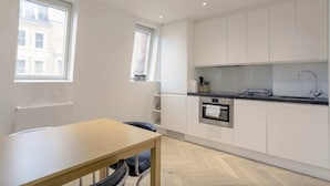 A modern kitchen with white cabinets, a built-in oven, and a window providing natural light. - Elegant 1 Bedroom Apartment in South Kensington (London)