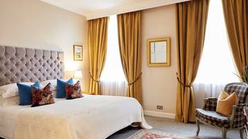 A bedroom with a tufted headboard, a large bed with white bedding and decorative pillows, a chair with plaid upholstery, and a patterned rug.