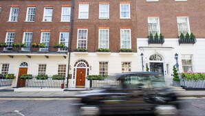 A row of traditional brick townhouses with white facades, each with a balcony and flower boxes. - 9 Hertford Street Mayfair (London)