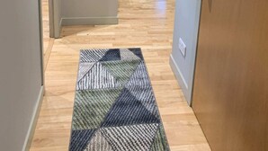 A hallway with a patterned rug, a framed certificate on the wall, and a blue sofa in the background. - Bright, Modern Apartment - Royal Mile (Edinburgh)