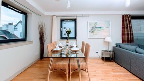 A modern living room with a glass dining table, wicker chairs, a grey sofa, and a small side table. - Bright, Modern Apartment - Royal Mile (Edinburgh)