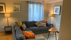 A living room with a grey sofa, orange cushions, a small table, and two floor lamps. - Bright, Modern Apartment - Royal Mile (Edinburgh)