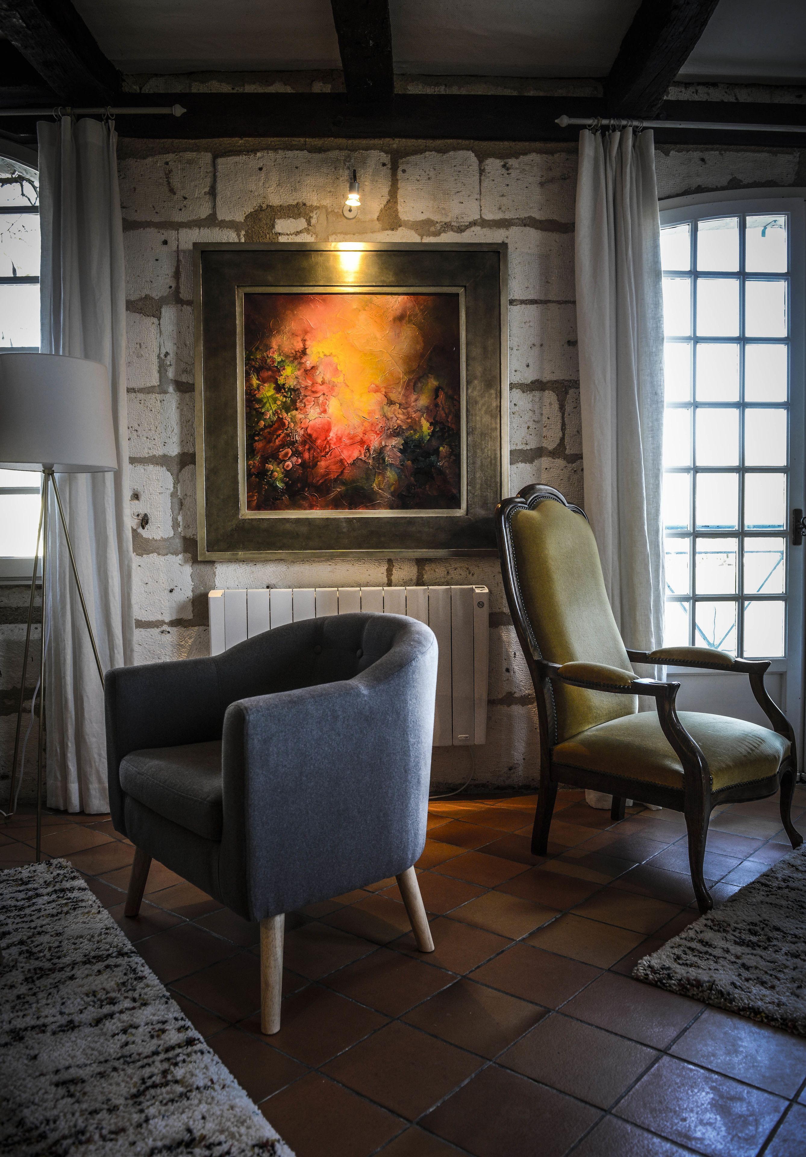 Una habitación con chimenea, dos sillones, una lámpara de pie y un cuadro grande en la pared.