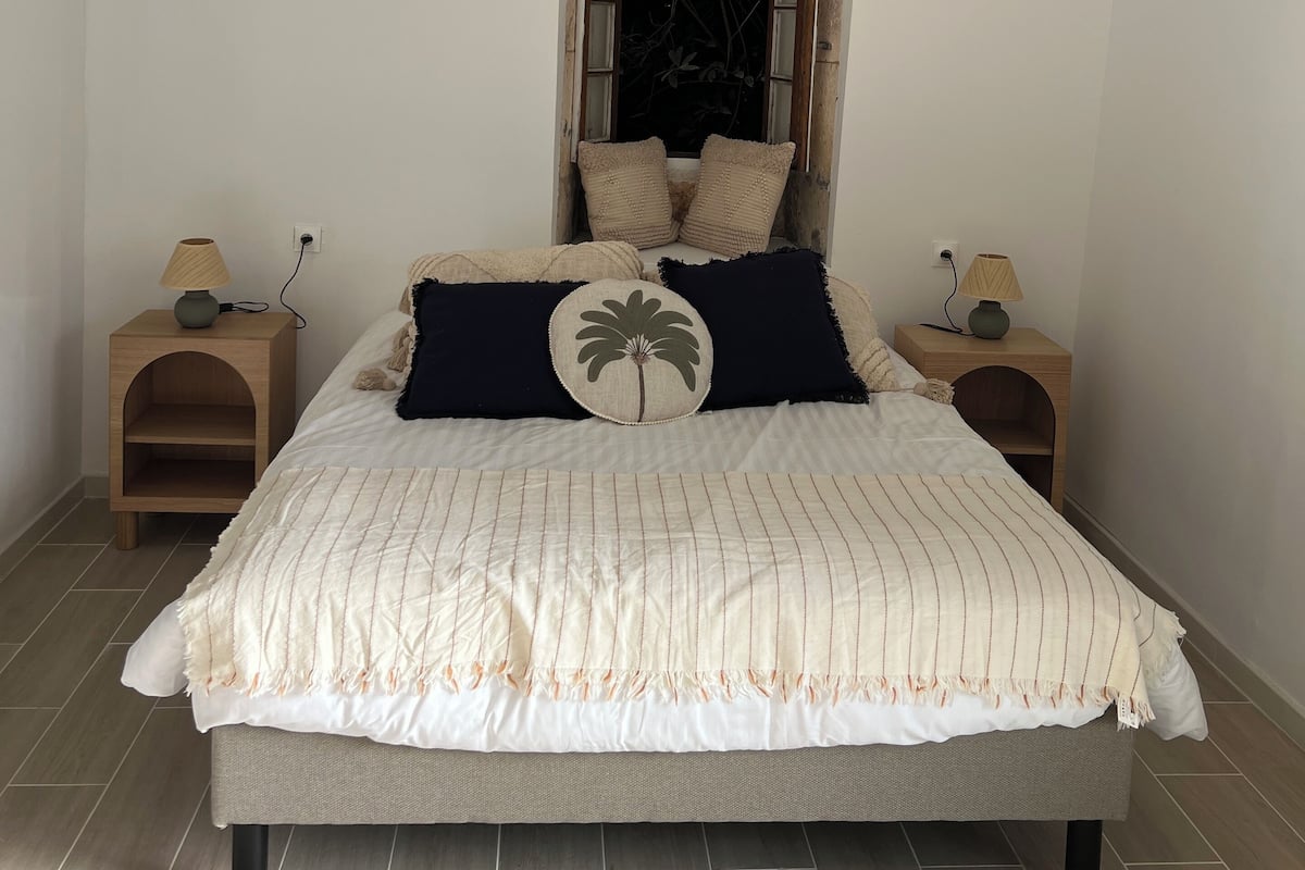 A bedroom with a bed, two nightstands, a window, and a view of the outdoors.