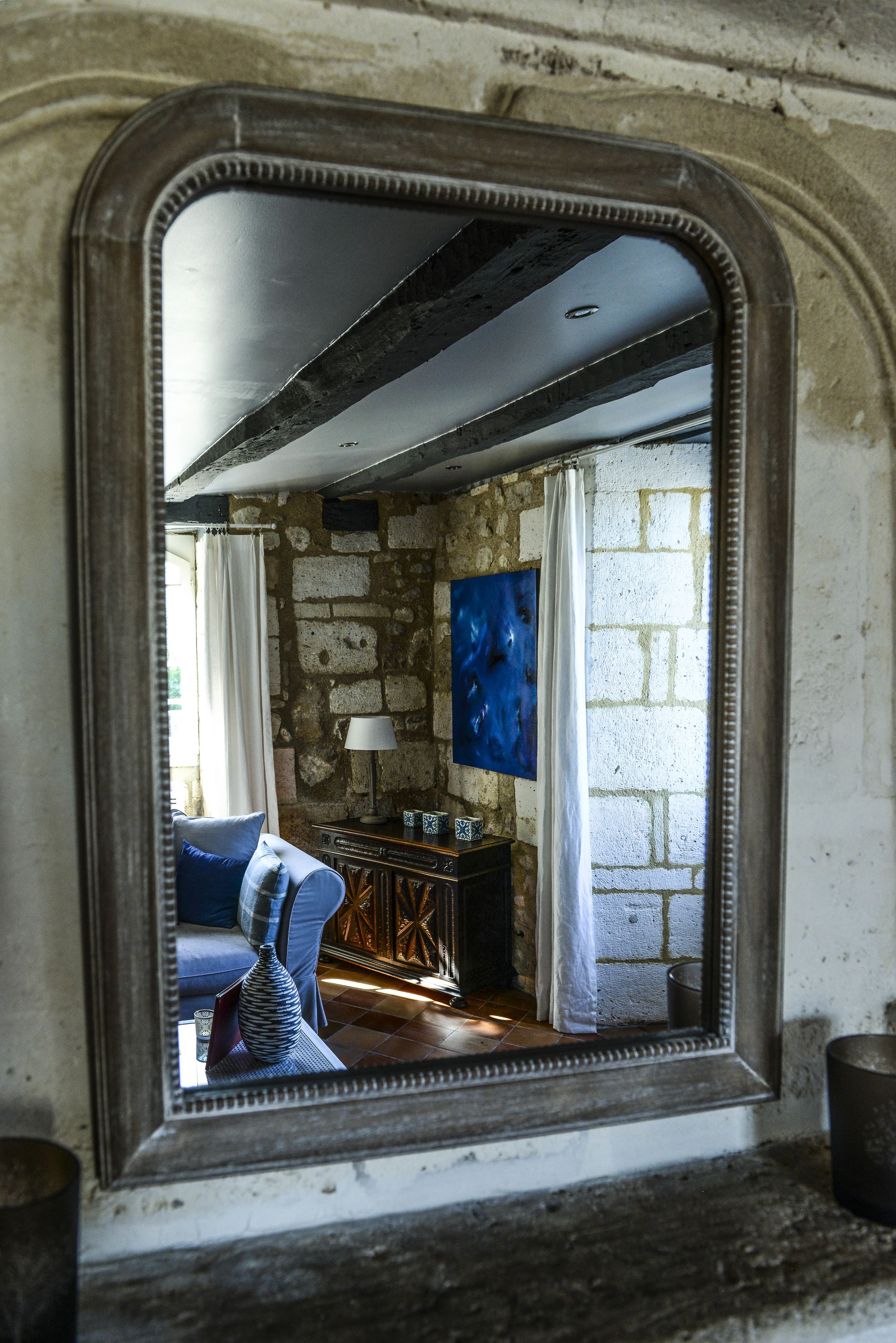 A mirror reflecting a room with a stone wall, a blue painting, a lamp, and a blue sofa.