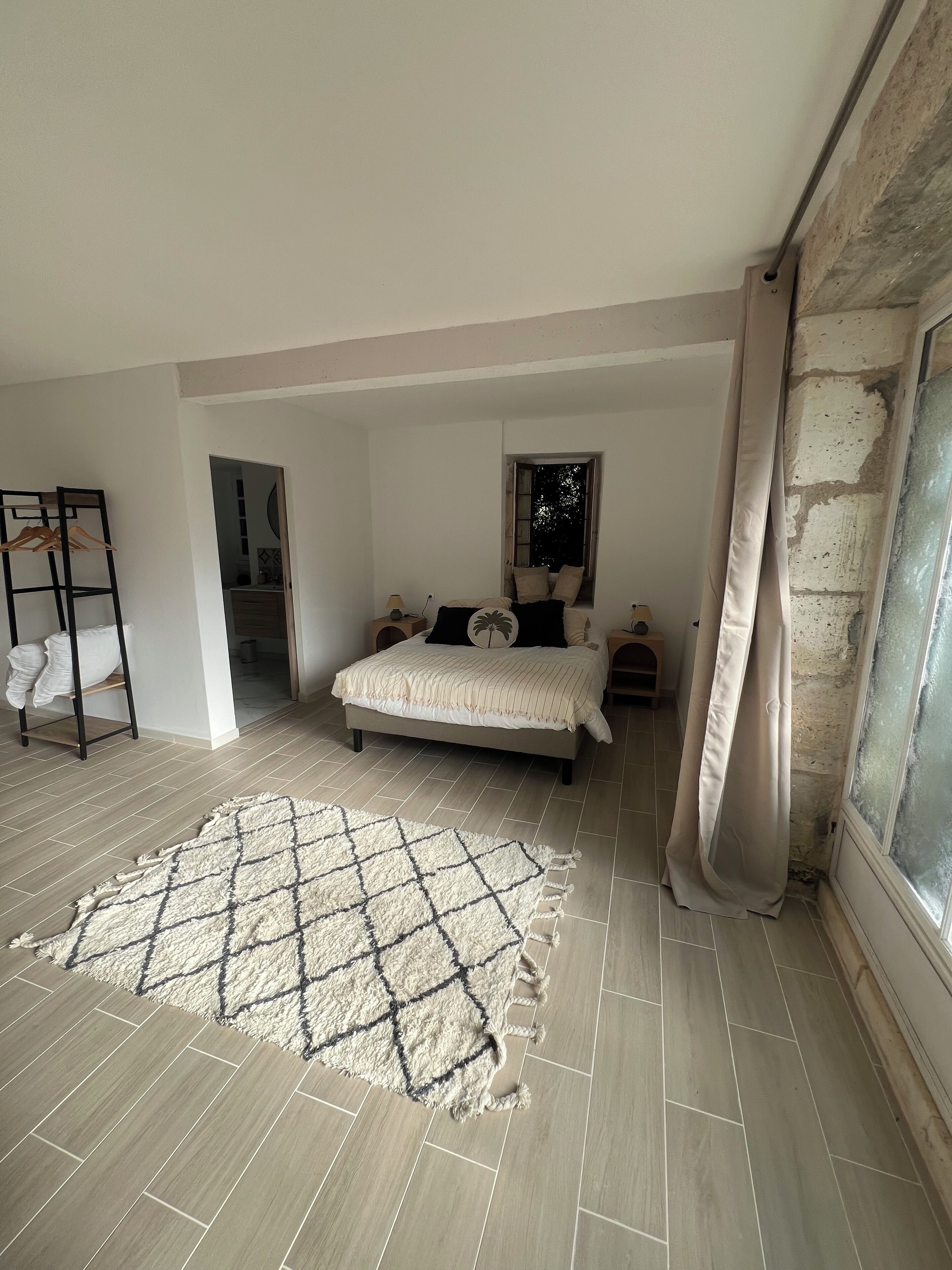 A bedroom with a bed, a wooden floor, a rug, a wardrobe, and a window with curtains.