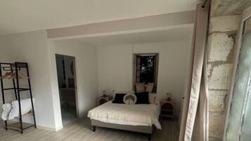 A bedroom with a bed, a wooden floor, a rug, a wardrobe, and a window with curtains.