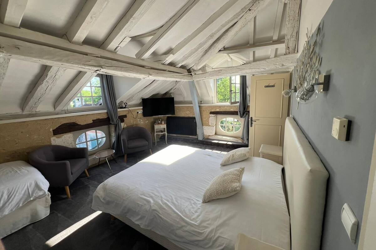 A bedroom with a large bed, a chair, a desk, a television, and a window.