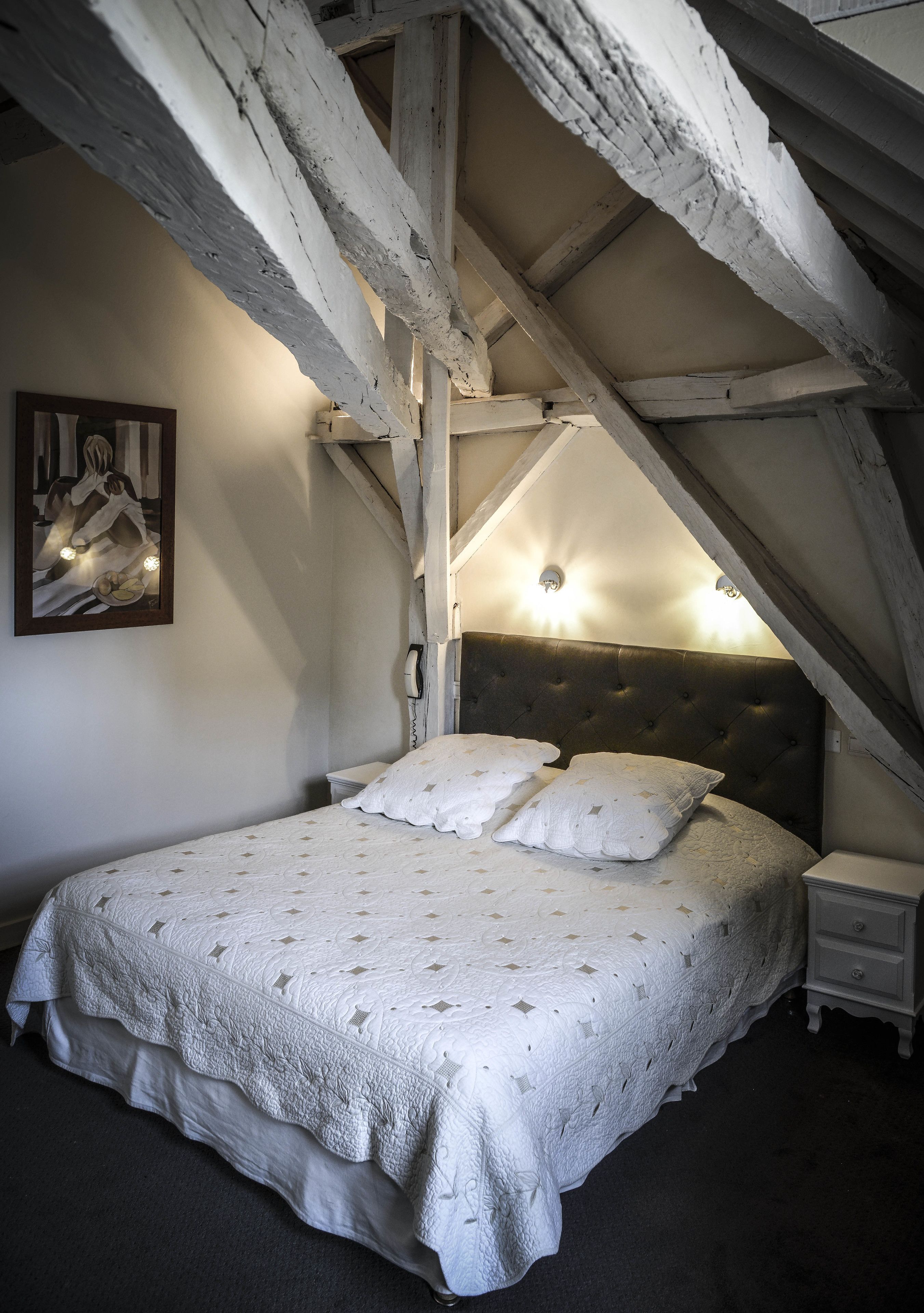 A bedroom with a large bed, a headboard, a bedside table, a nightstand, a wall-mounted phone, and a painting on the wall.