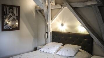 A bedroom with a large bed, a headboard, a bedside table, a nightstand, a wall-mounted phone, and a painting on the wall.