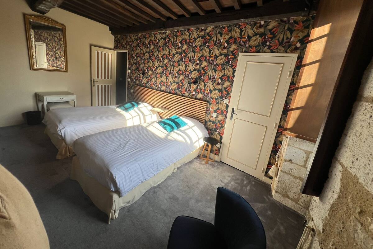 A bedroom with two beds, a wooden headboard, a small stool, a white wardrobe, and a mirror on the wall.