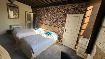 Un dormitorio con dos camas, un cabecero de madera, un taburete pequeño, un armario blanco y un espejo en la pared.