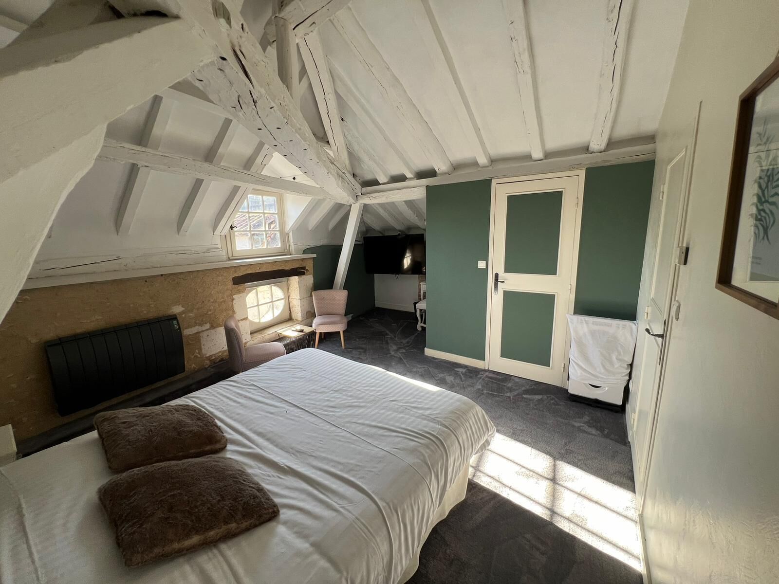 Een slaapkamer op zolder met een groot bed, een stoel, een kleine tafel en een raam.