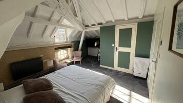 Un dormitorio en el ático con una cama grande, una silla, una mesita y un ventanal.