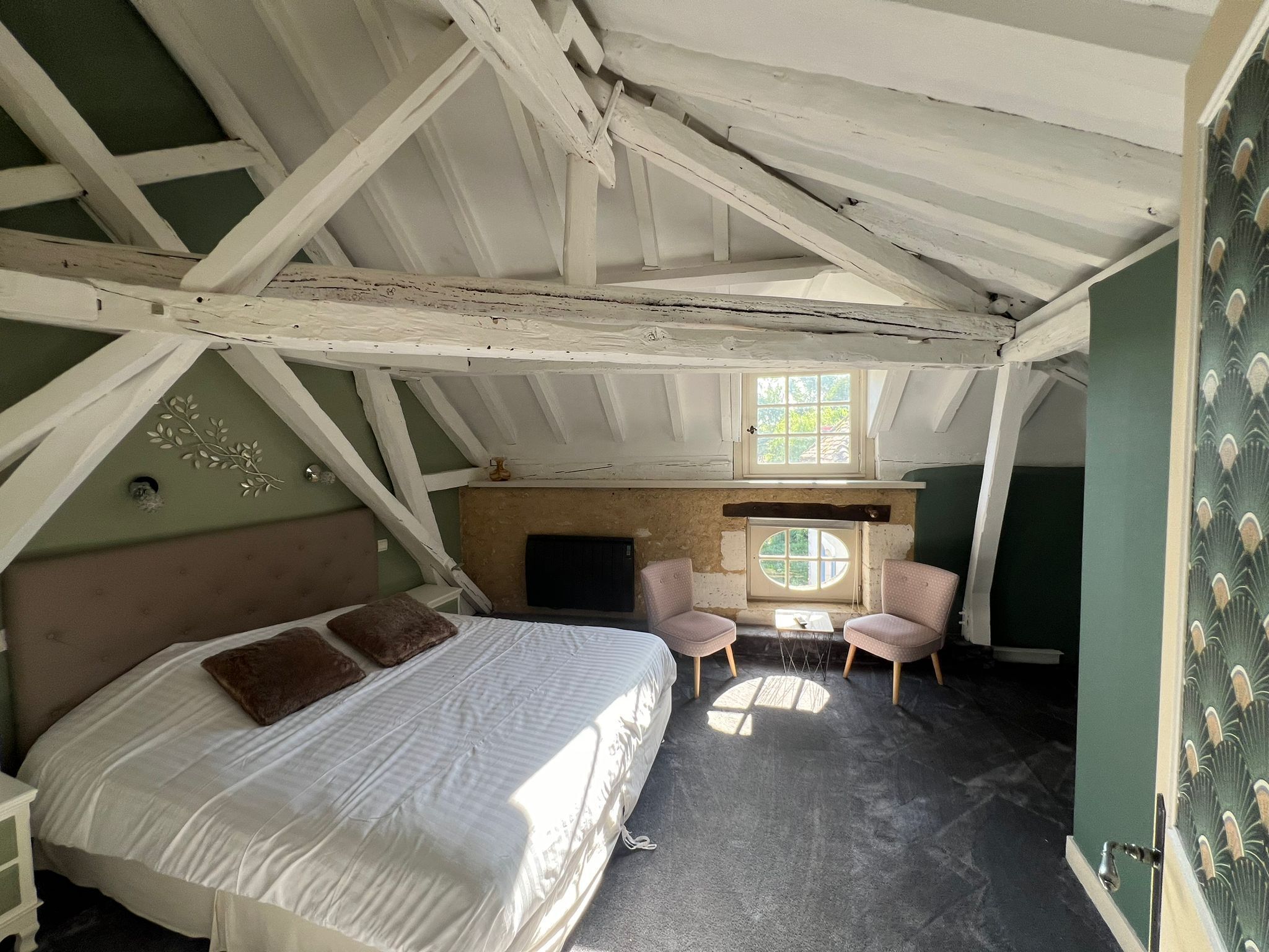 A bedroom with a bed, two chairs, a fireplace, and a window.