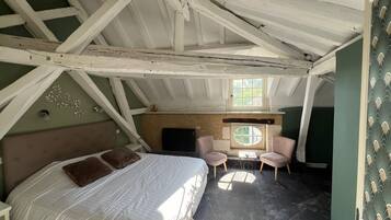 A bedroom with a bed, two chairs, a fireplace, and a window.