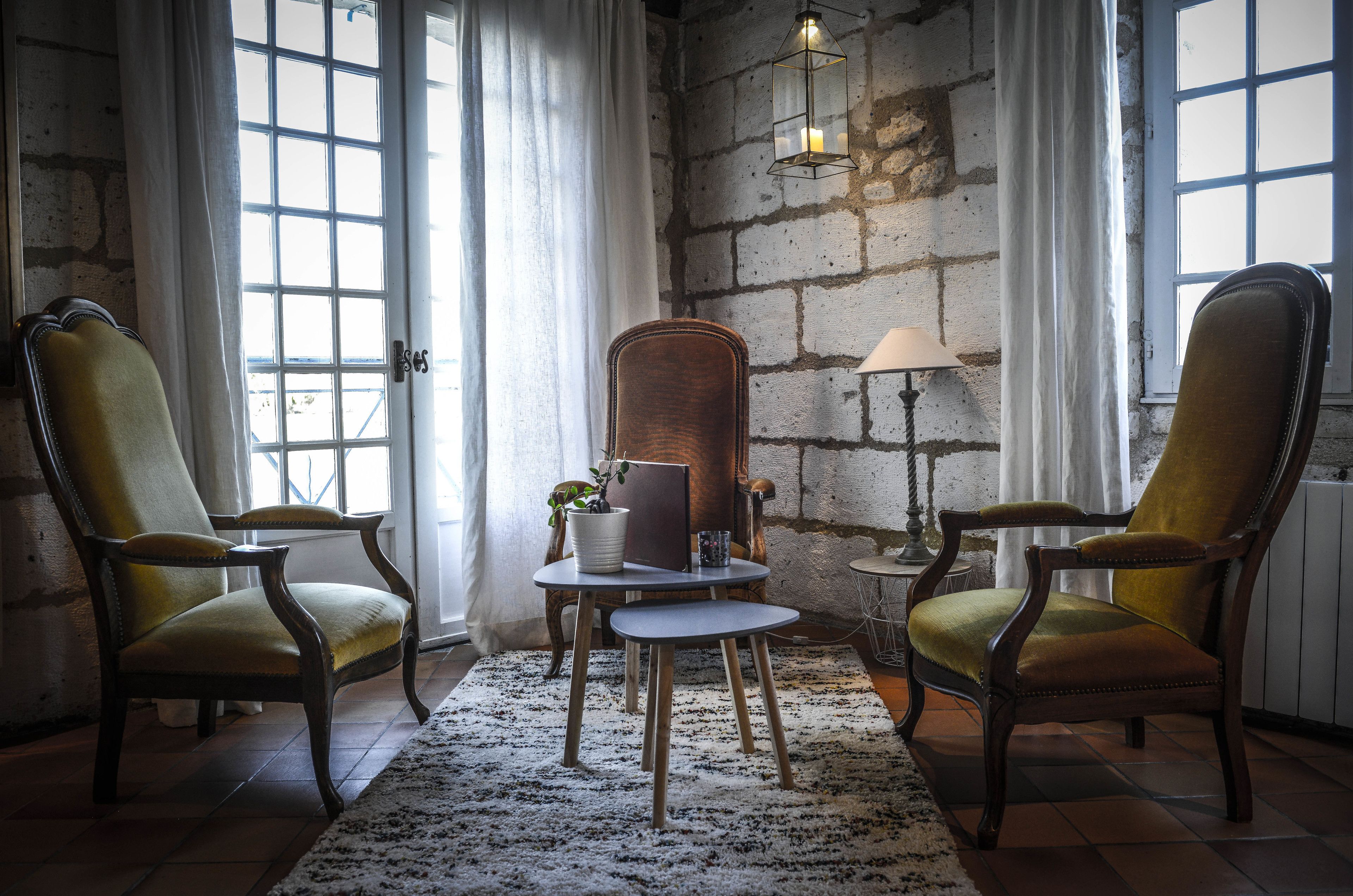 A room with two wooden armchairs, a small round table with a potted plant, and a lamp.