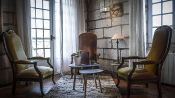 A room with two wooden armchairs, a small round table with a potted plant, and a lamp.