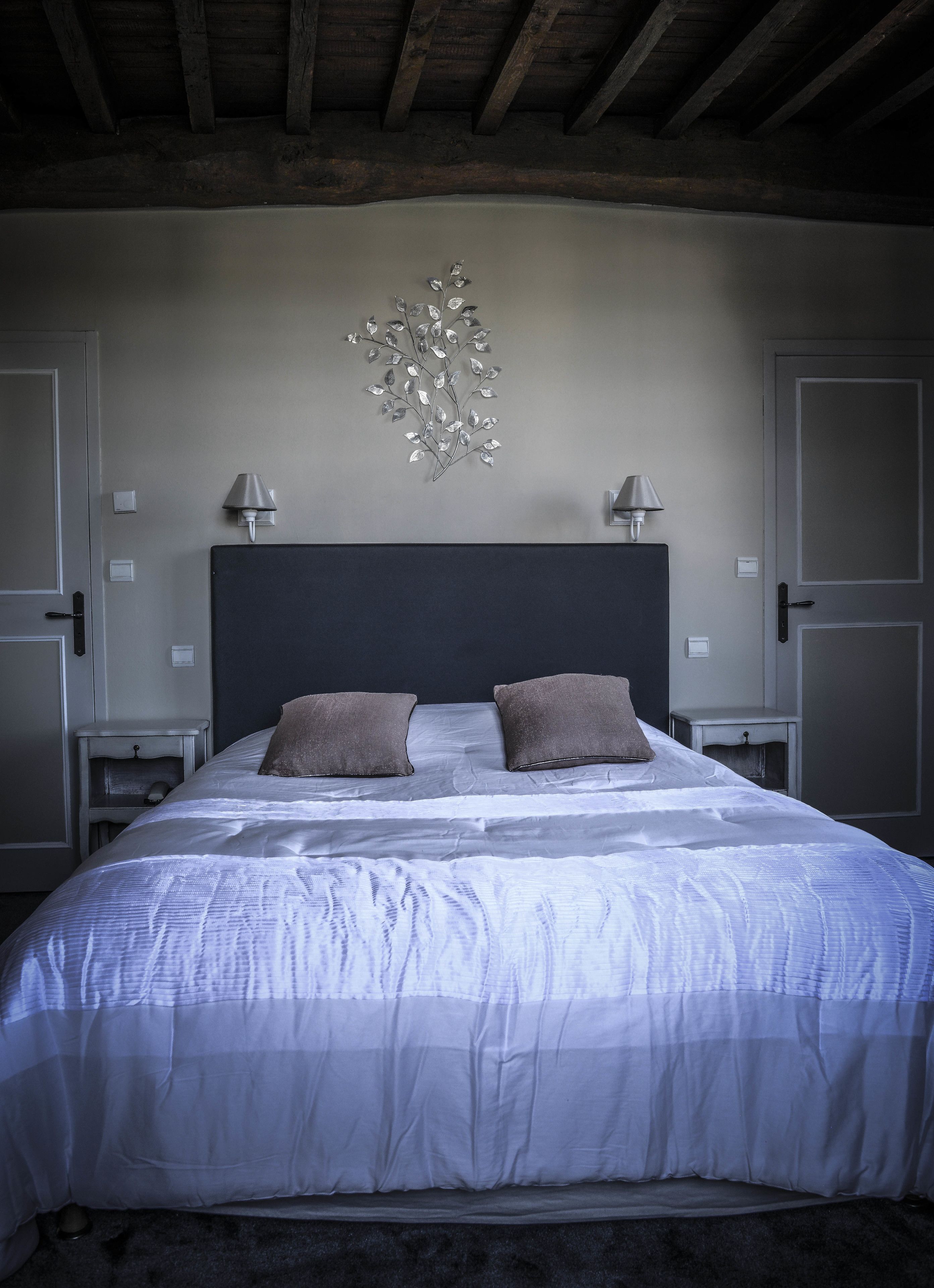 A bedroom with a large bed, two bedside lamps, a decorative wall piece, and a dark headboard.