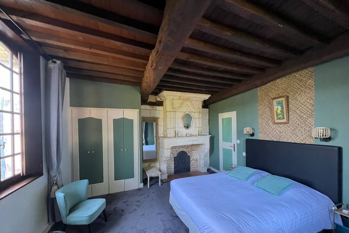 A bedroom with a bed, a chair, a fireplace, and a wardrobe.
