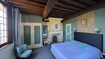 A bedroom with a bed, a chair, a fireplace, and a wardrobe.