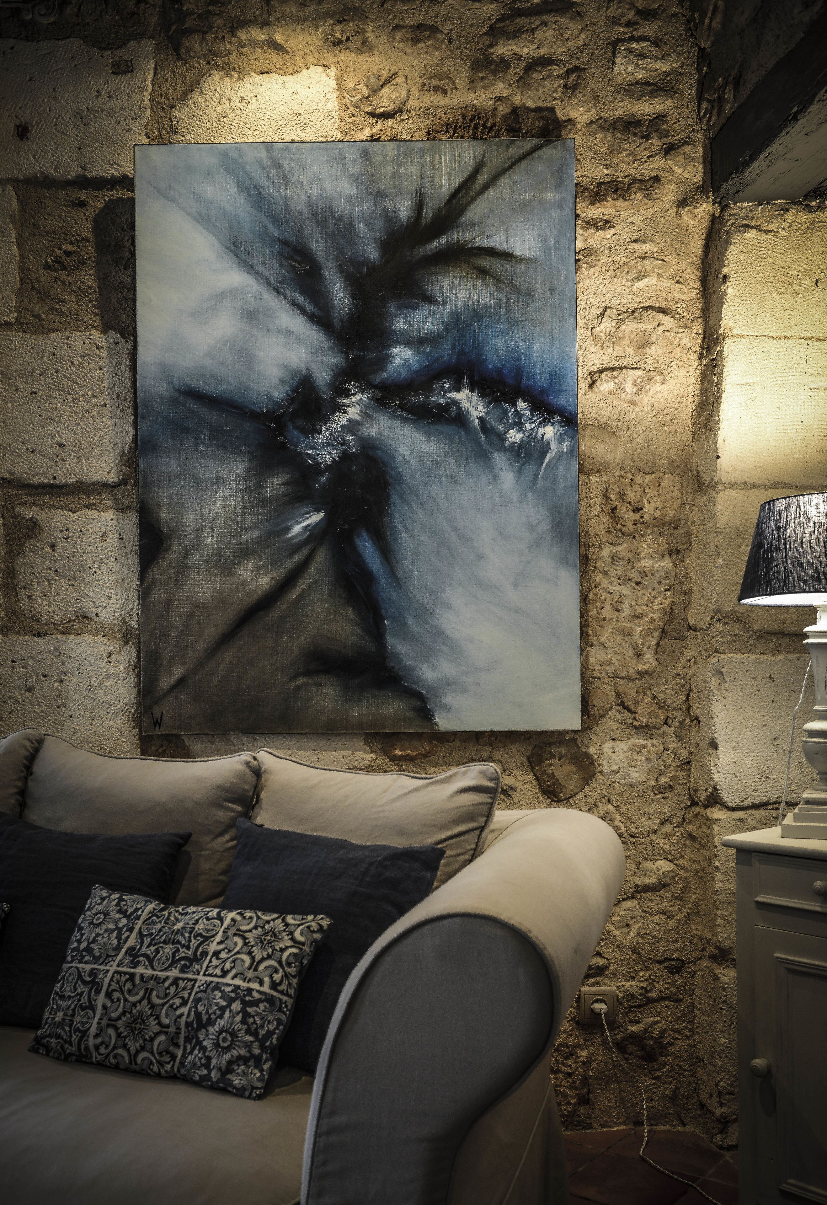 A room with a stone wall, a painting, a sofa, and a lamp.