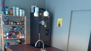 A compact kitchen with a wooden countertop, a stainless steel sink, and a refrigerator. There are two stools and a hanging light fixture. - Central Apartment for the Fringe (Edinburgh)