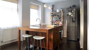 A kitchen with a wooden island, bar stools, a refrigerator, and a shelf with various items. - Central Apartment for the Fringe (Edinburgh)