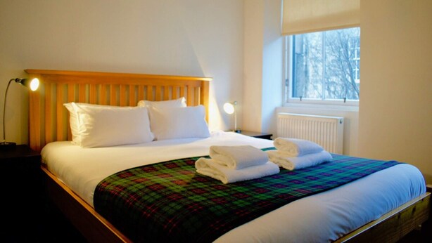 A neatly made bed with white linens, a plaid blanket, and folded towels. - Central Apartment for the Fringe (Edinburgh)