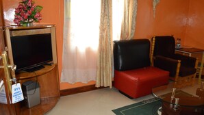 Une chambre d’hôtel équipée d’un téléviseur à écran plat, d’un canapé rouge, d’une table basse en verre et d’une petite table d’appoint avec une bouteille.