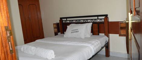 Una cama bien hecha con un cojín que dice "ABBEY RESORT" en una habitación con muebles de madera y una alfombra verde.