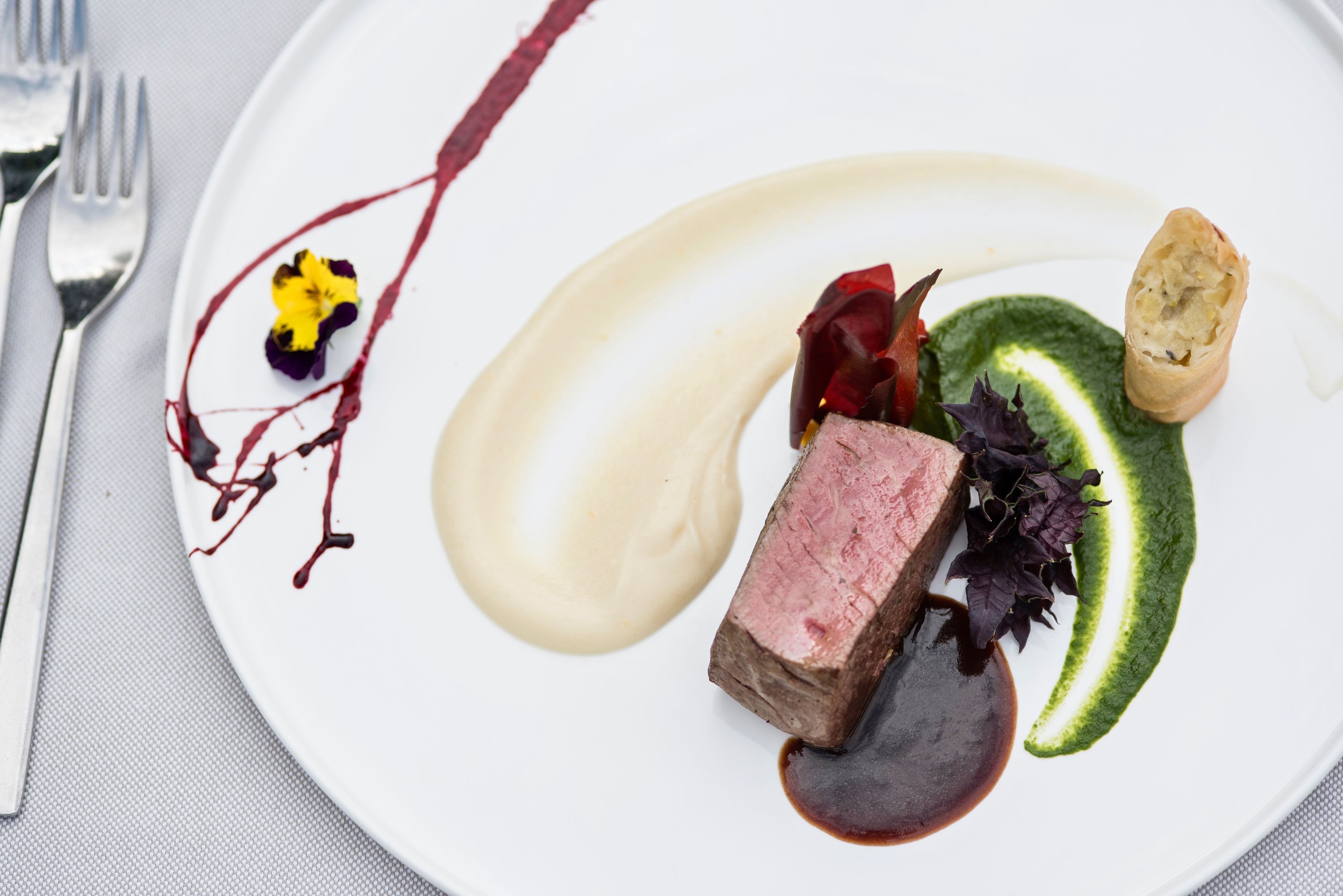 Une assiette avec un steak, une sauce verte et une petite fleur.