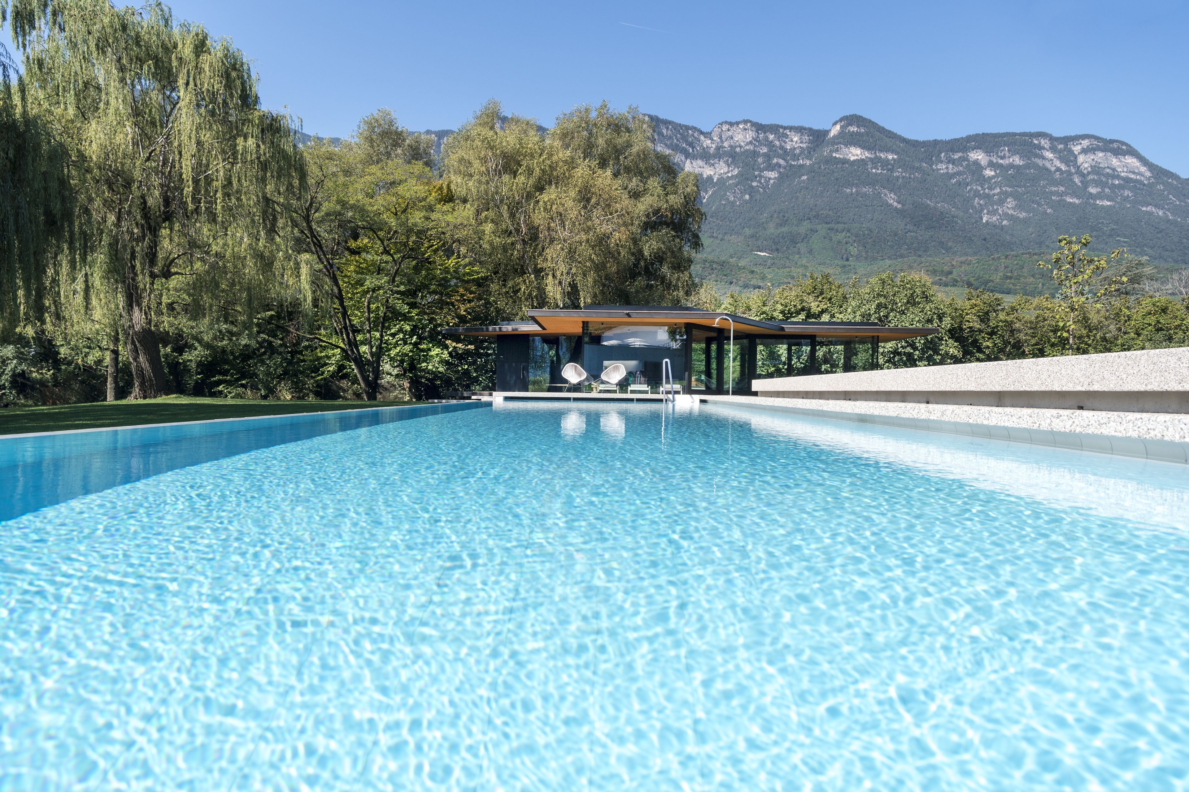 Uma piscina com área envidraçada, cercada por árvores e montanhas ao fundo.