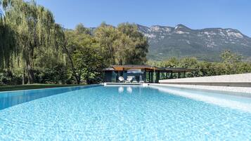 Uma piscina com área envidraçada, cercada por árvores e montanhas ao fundo.
