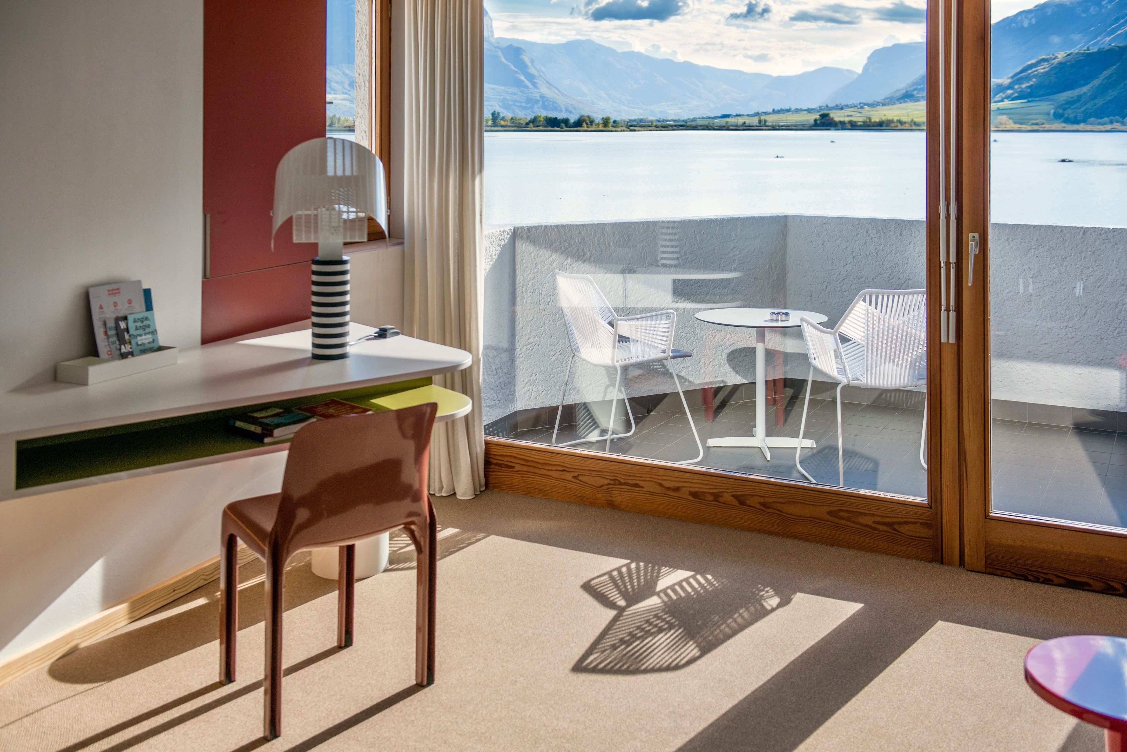 Une chambre moderne équipée d’un bureau, d’une chaise et offrant une vue sur un lac et des montagnes grâce à une grande fenêtre.