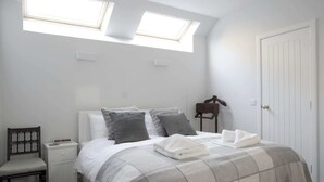 Una camera da letto con un letto, una sedia, un comodino, un armadio e lucernari.