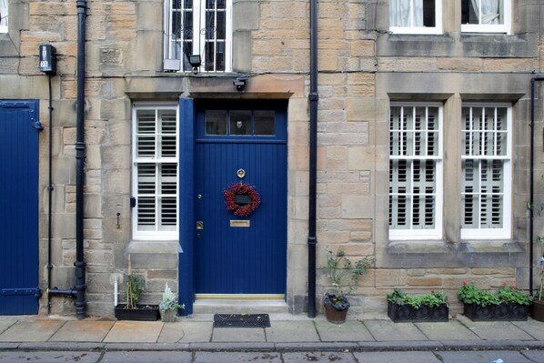 A stone building with a blue door, white window shutters, and potted plants on the ground.